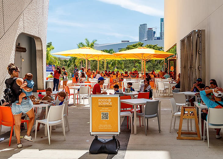 Outdoor dining areas at the Frost Museum in Florida where QR codes are seen for information and menu access.