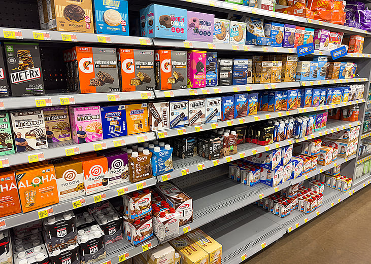 Shelves stocked with protein bars in a grocery store.