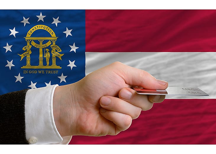 A person's hand holding a credit card with a background of US state Georgia's flag.