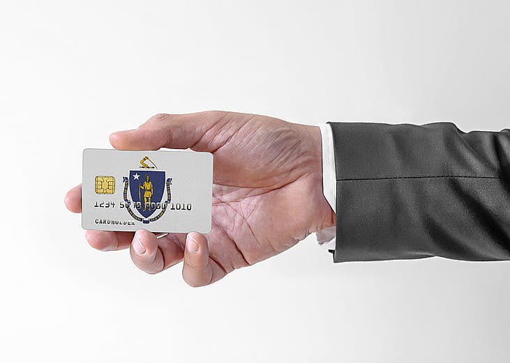 A person's hand holding a credit card designed with the flag of Massachusetts.