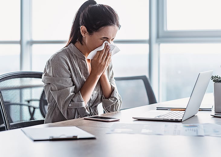 A sick businesswoman blowing her nose at work.