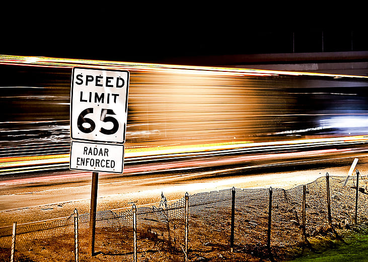 65 mph speed limit sign with a background of long exposure trails.