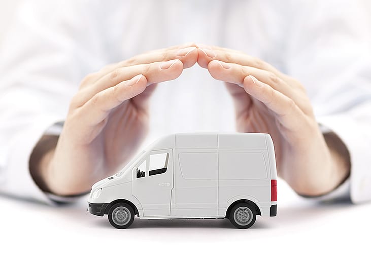 A figure of a small transport van protected by hands of a car insurance agent.