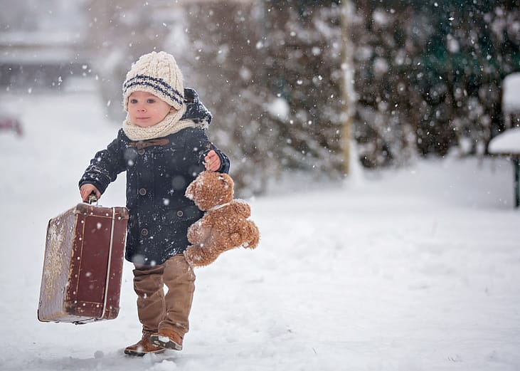 Baby playing with teddy bear in the snow.