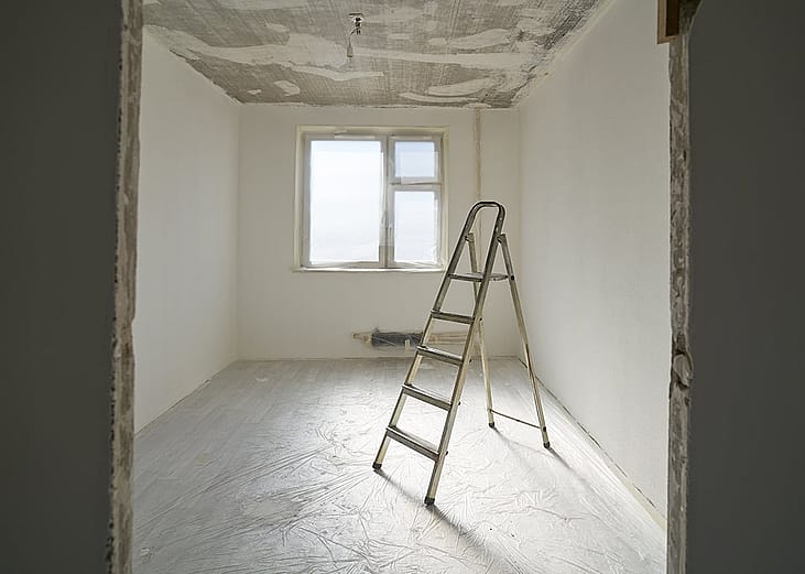 A ladder at the center of an apartment room with unfinished interior paint. 