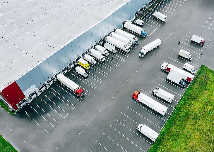 Aerial view of logistic trucks lined up at the loading docks of a large distribution warehouse.