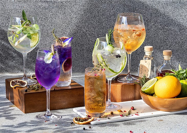 A display of assorted homemade herbal cocktails in wine glasses.