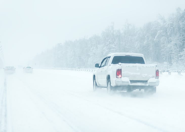 Rear view of a white pickup truck on the road during heavy snowfall.