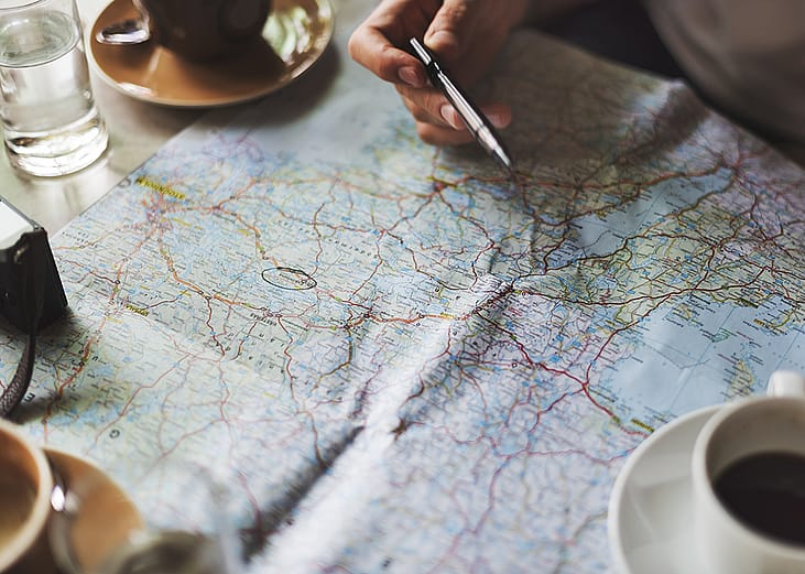 Person tracing a map with a pen for travel planning.