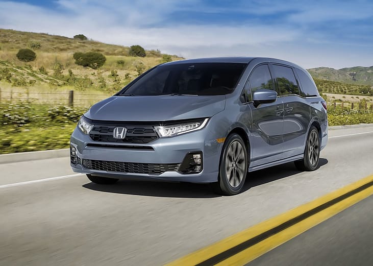 A dark gray Honda Odyssey driving down a rural road. 