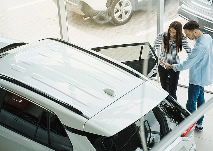 A young couple checking out a car at a dealership.