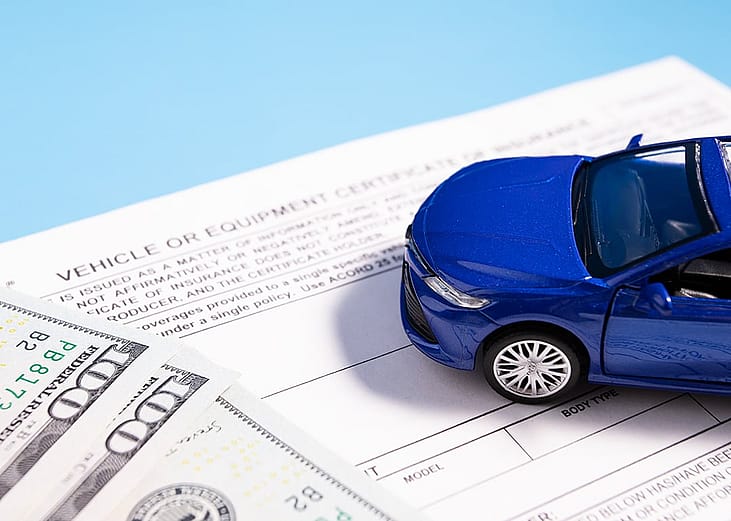 A small figure of a blue car on top of banknotes and insurance documents.