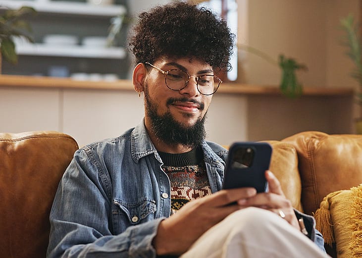 A young man smiling while typing on a smartphone.