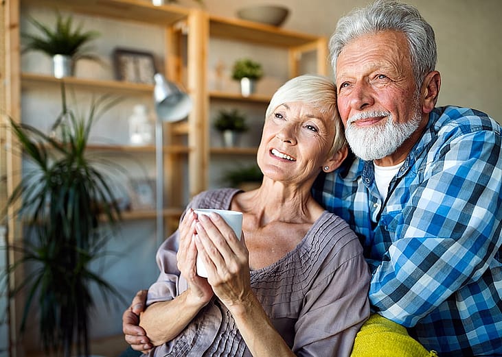 A senior couple hugging and looking out while having a coffee in the morning.
