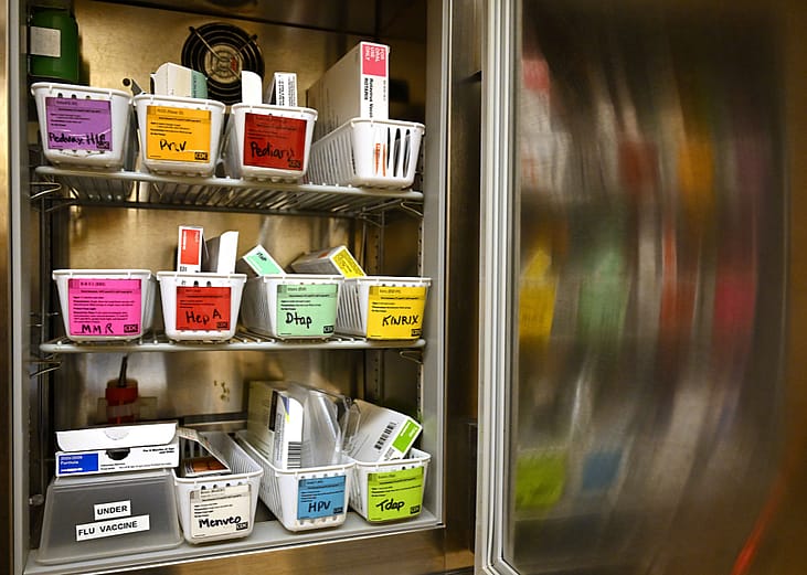 A small open refrigerator with shelves of baskets of vaccines at a health clinic.