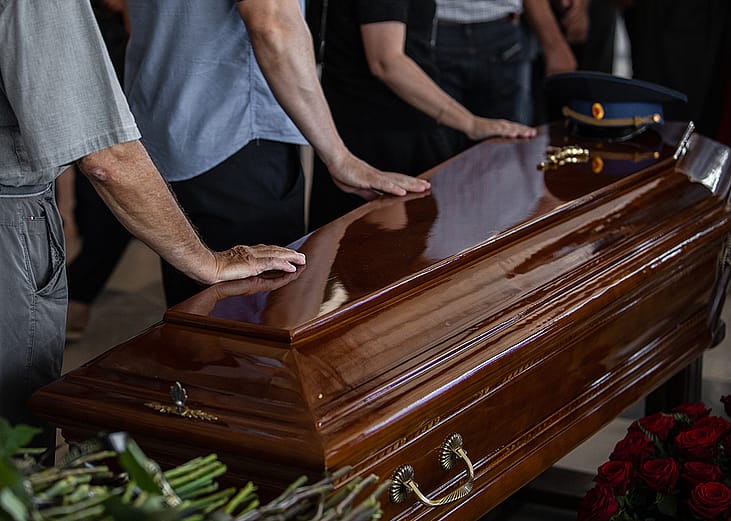 People touching the wooden brown coffin of a deceased relative.