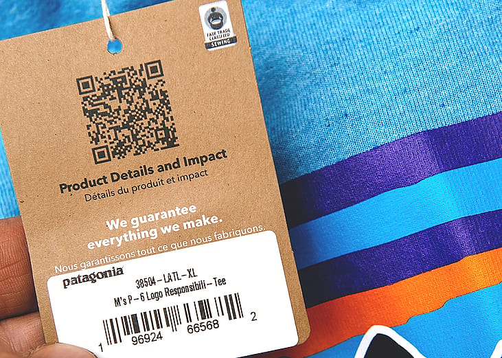 A product tag on a blue clothing shirt with QR code for product details and impact.