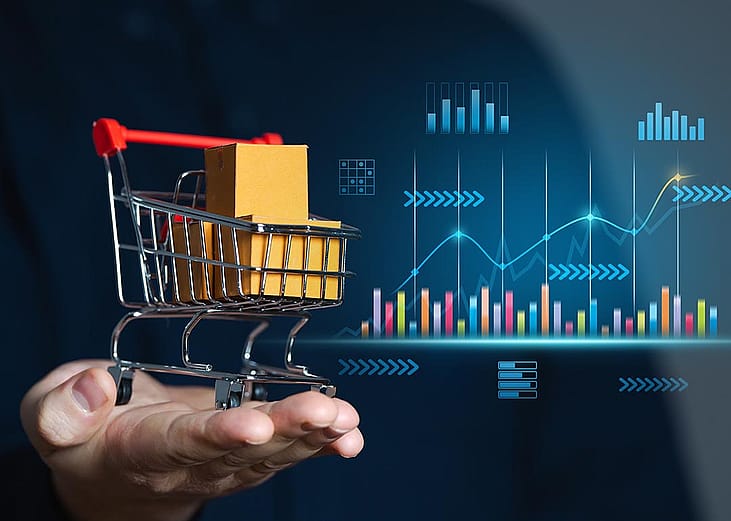 Concept of retail sales illustrated by perosn holding miniature shopping cart with packages inside; chart with growth figures and data in the background 