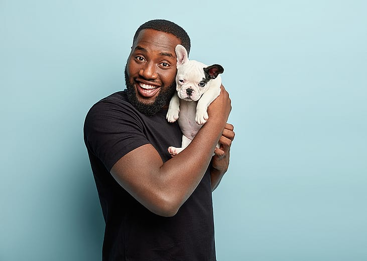 A young black man happily posing with his french bulldog puppy.