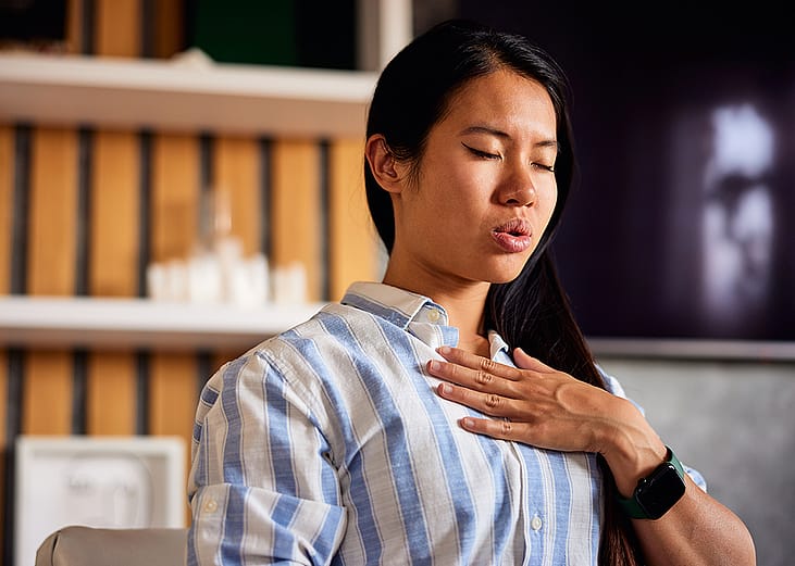 A young woman with her hand on her chest, practicing a breathing technique at home.