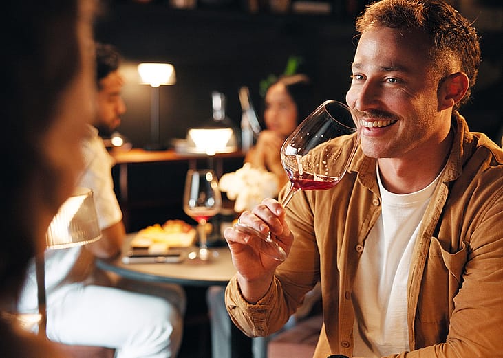 A man facing his date and drinking a glass of wine during their restaurant dinner.