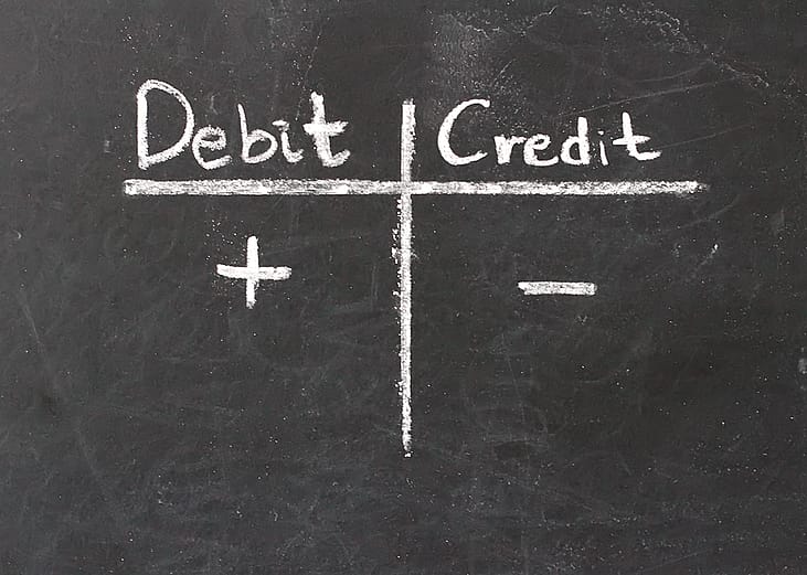 A chalkboard with 'Debit' and 'Credit' written in a table with plus and minus symbols.