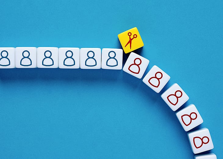 A scissor symbol on a block cutting through a row of human figures as a concept of mass layoffs.