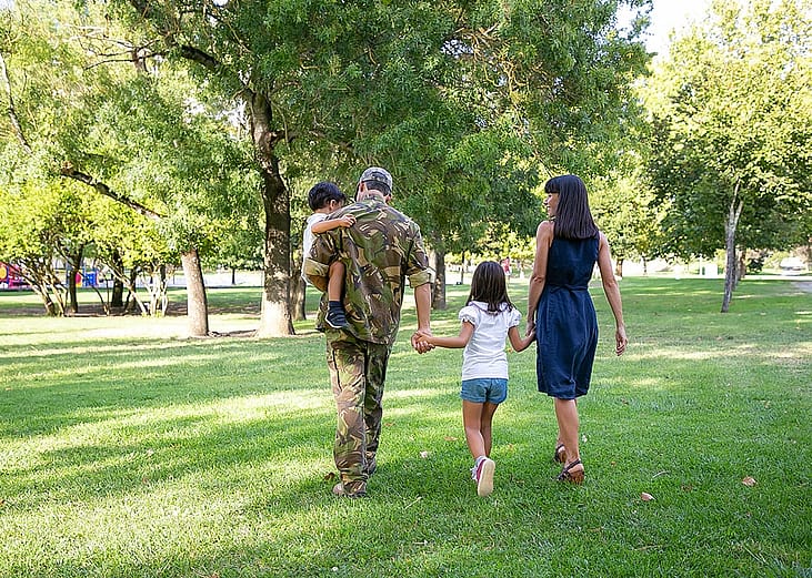 Back view of happy family walking together in a park. The father is wearing camouflage military uniform.