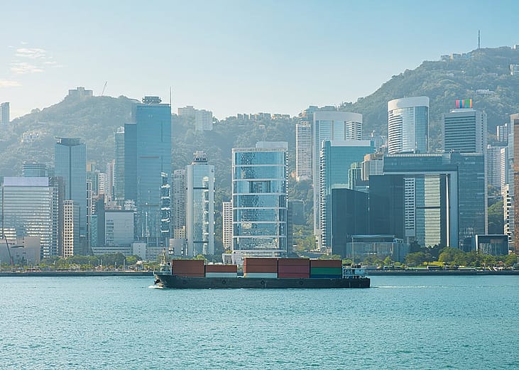 A cargo ship on the Victoria Harbour with the Hong Kong skyline in the background.