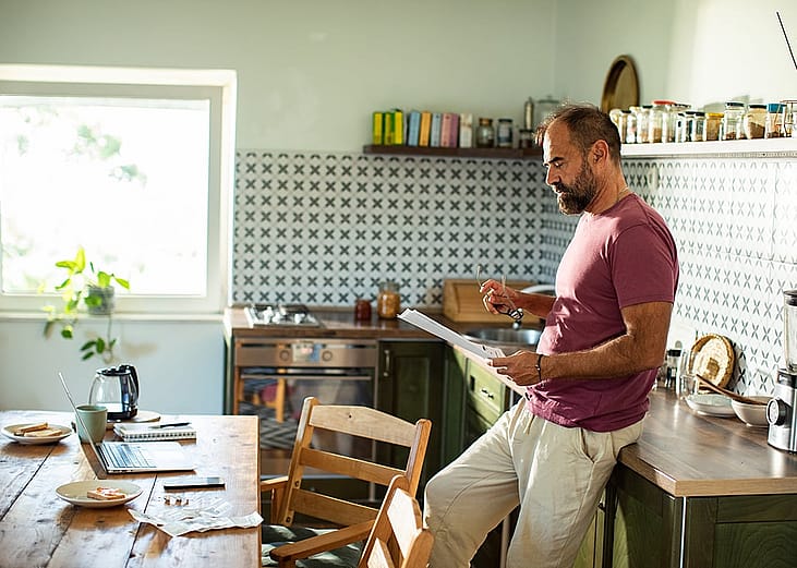 A man reading a utility bill in the kitchen at home.
