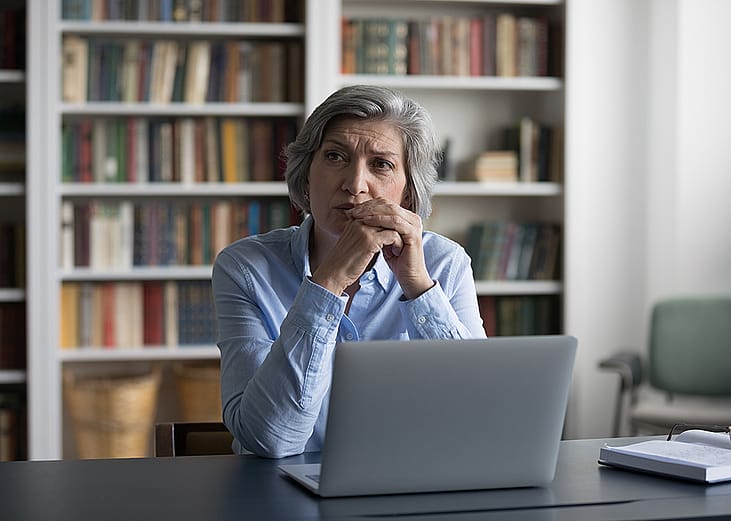 A pensive middle-aged woman thinking while sitting at a table in an office.