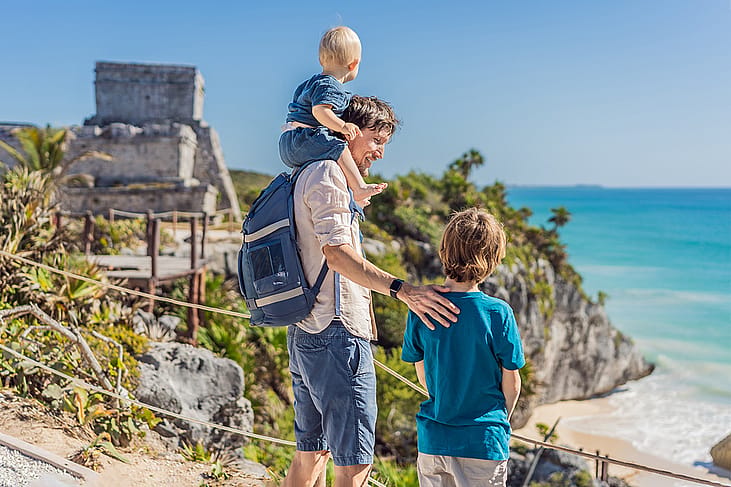 A father with his two sons enjoying the view of the pre-Columbian Mayan walled city of Tulum in Mexico.