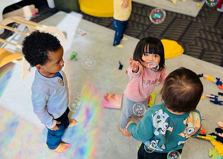 Young children playing with bubbles in day care. In the U.S., families spend between nine percent and 16 percent of their median income on full-day care for just one child.