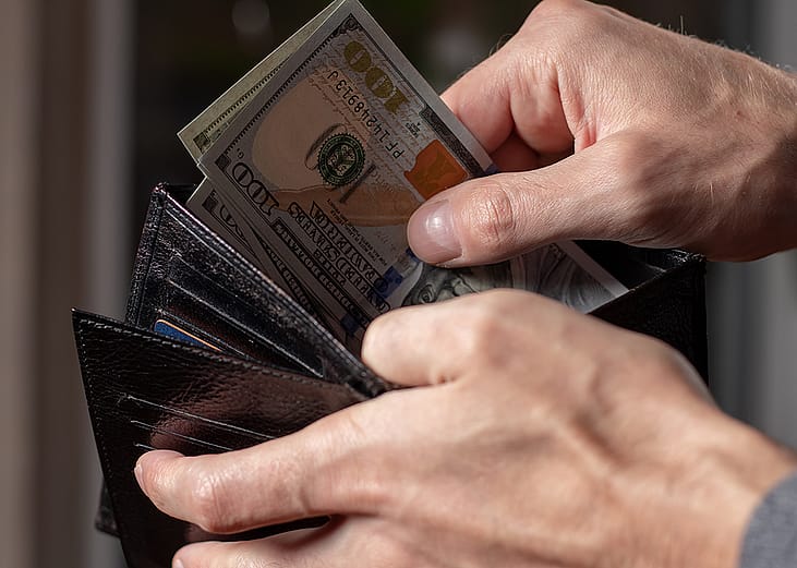 A person taking out dollar bills from a wallet.