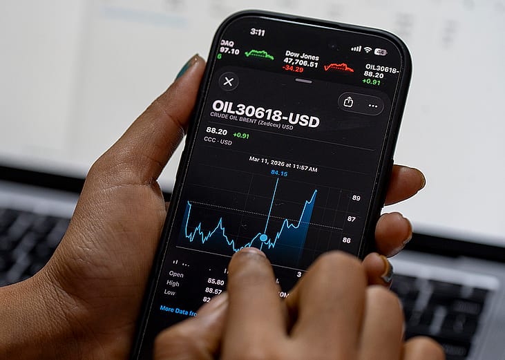 Person monitoring smartphone displaying Brent crude oil prices in USD.