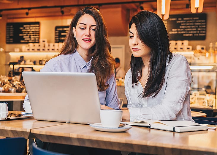 Two businesswomen at a cafe working on a project together.