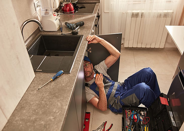 A plumber fixing a water pipe under the kitchen sink. 