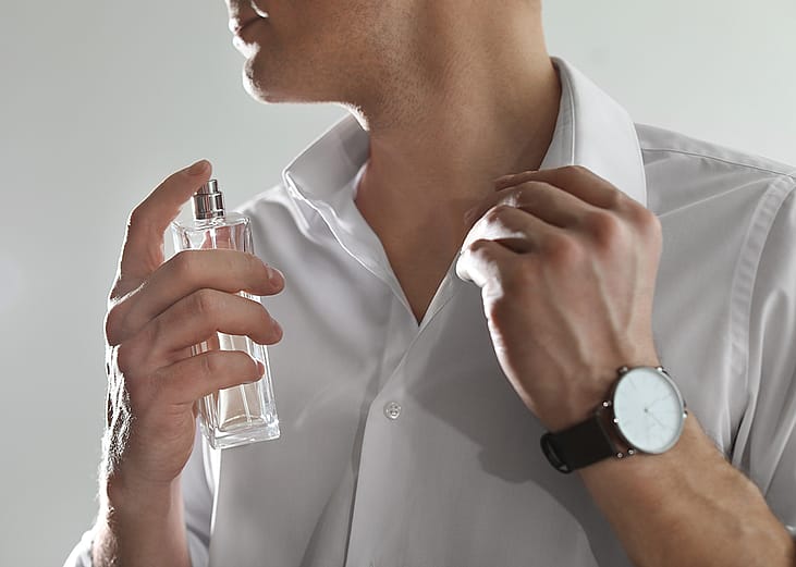 A close-up of a person applying a perfume in his neck. 