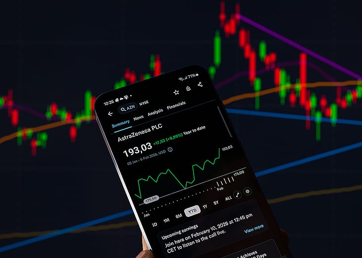 The AstraZeneca stock graph displayed on a mobile phone with other stock charts in the background.