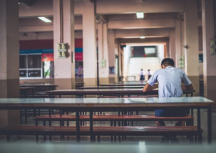 A male high school student sitting alone at a cafeteria.