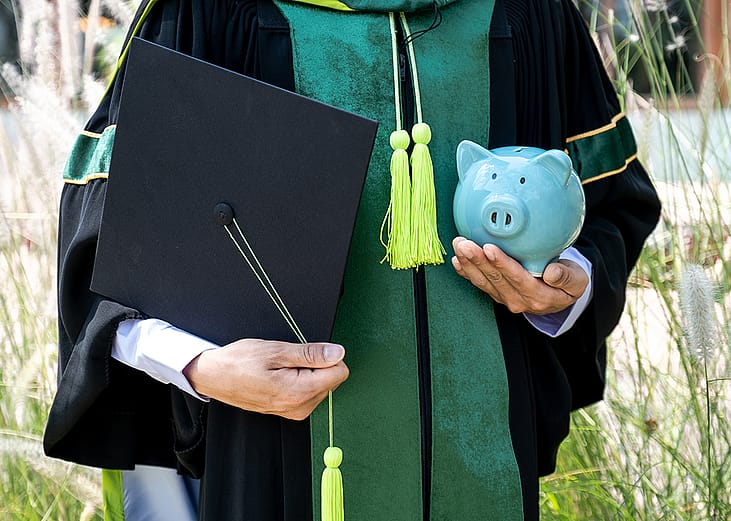 A person wearing a bachelor uniform holding a cap and a piggy bank.