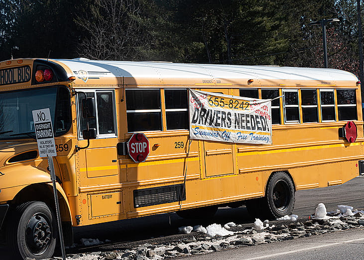 A school bus with a hanging display of drivers needed during a driver shortage in Windsor, New York, USA.