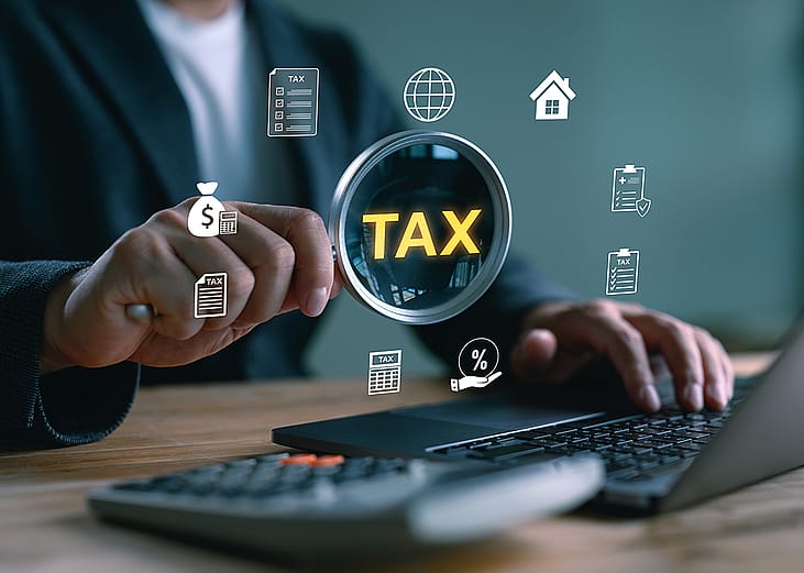 'Tax' and related graphics illustrated over a magnifying glass focusing on a computer as a concept of tax filing.