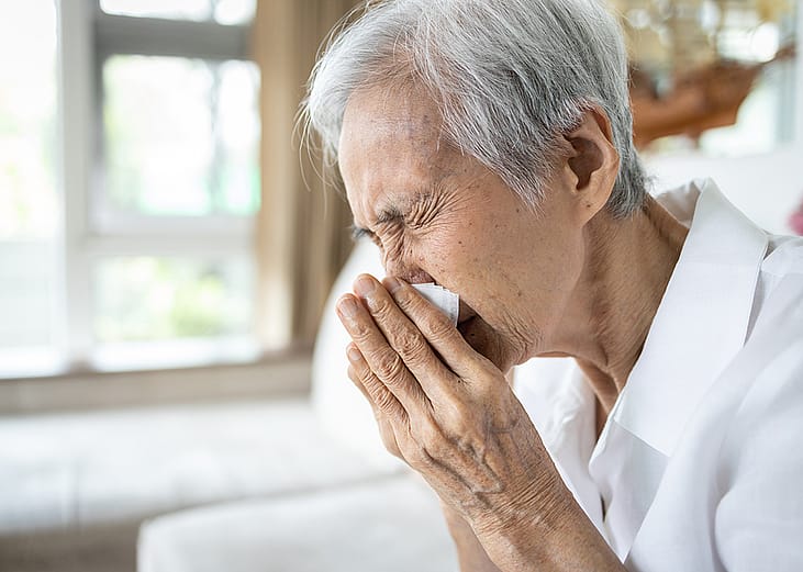 An elderly person blowing her nose after a sneeze.