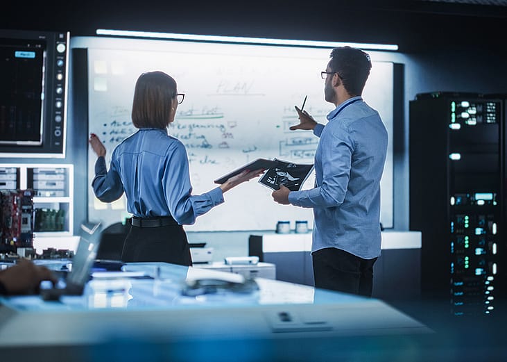 A team of two professional engineers using a digital tablet to discuss a manufacturing plan.
