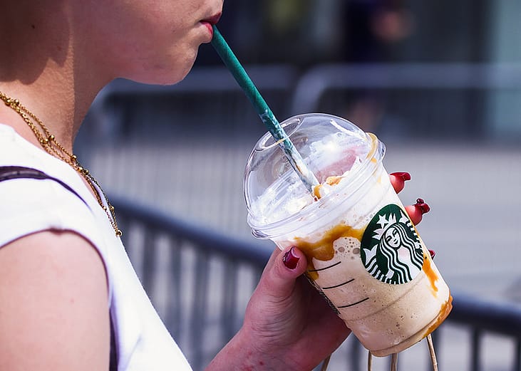 A person drinks Starbucks iced coffee outside.