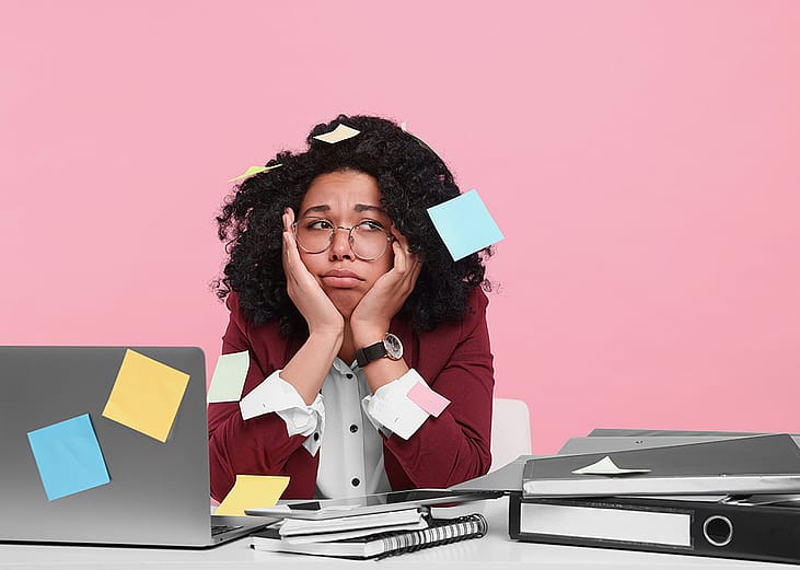 A young woman with sticky notes taped around her looking stressed at work.