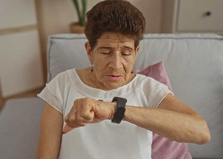 A senior woman observing her smartwatch while sitting on a sofa at home.