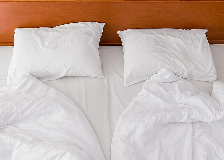 A view from above of an unmade bed with two duvets and white pillows.