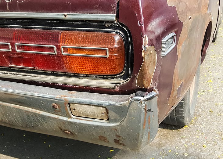 A close-up shot of the back of an old rusty car. 
